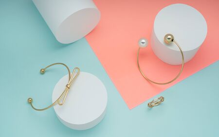 Golden bracelets and golden ring on pastel colors background - Bow design and pearl golden bracelets on pink and green backgroundの写真素材