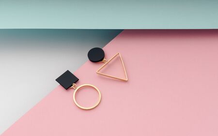 Geometric shapes stud earrings pair on pink, blue and white paper backgroundの写真素材