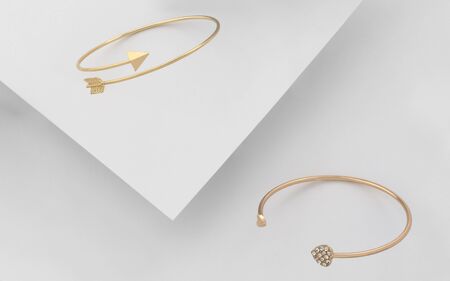Golden arrow and heart shape bracelets on white background. Modern design golden bracelets on white paperの写真素材