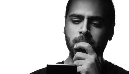 Black and white portrait of middle eastern guy looking at his phone and thinking on white backgroundの写真素材