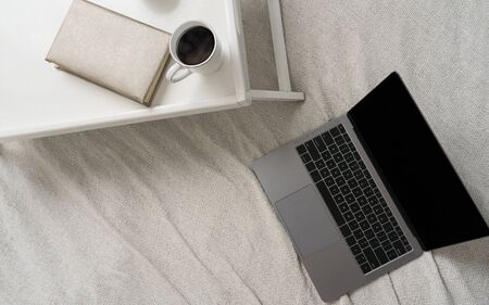Top view of coffee cup and book on bed table and Laptop on the bed