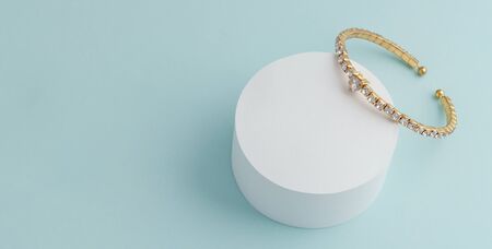 Diamond golden luxury bracelet on white round platform on blue background with copy spaceの写真素材