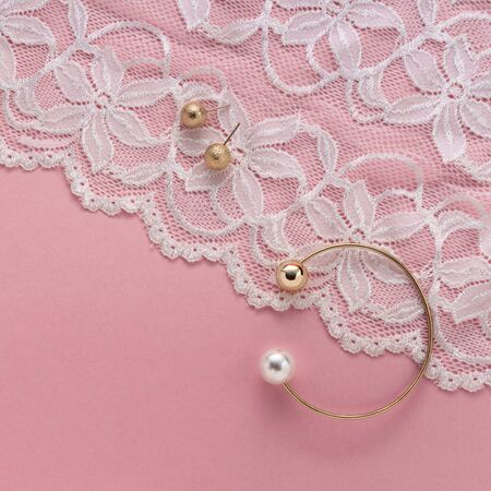 Pearl golden bracelet and stud earrings on white textile on pinkの写真素材