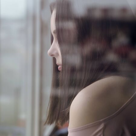 Close up on girls face behind the window looking outside during epidemic quarantineの写真素材