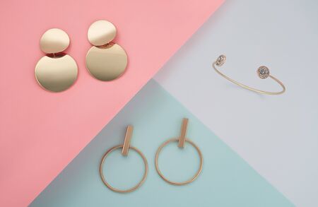 Top view of two modern pairs of earrings and bracelet on pastel color geometric backgroundの写真素材