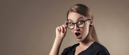 Portrait of surprised girl with open mouth wearing eye glasses on beige background with copy spaceの写真素材