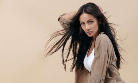 Portrait of brunette girl with healthy long hair on beige background with copy space