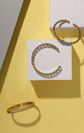 Top view of golden bracelets on white cubes on yellow background