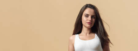 Portrait of young brunette woman on beige background with copy spaceの写真素材