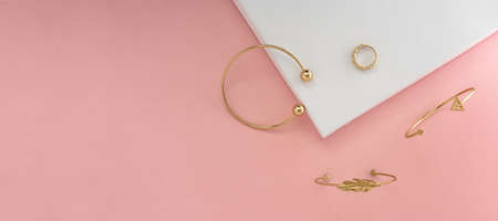 panoramic shot of golden jewelries on pink background with copy space