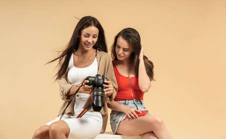 Two young women watching photos on professional camera on beige background