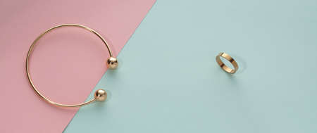 Top view of golden bracelet and ring on blue and pink paper with copy space