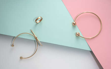 Top view of golden bracelets and ring on pink and blue papers background with copy space