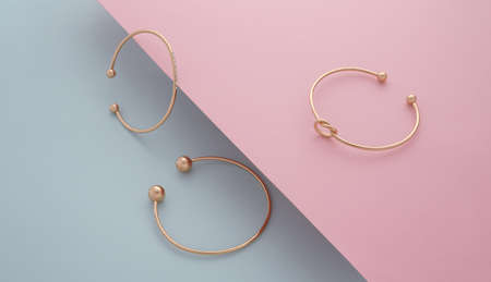Three golden bracelets on pink and blue slanted background