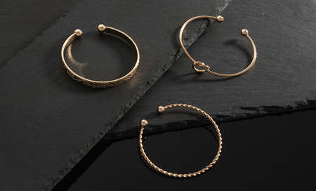 Three modern design golden bracelets on black stone plates on black background