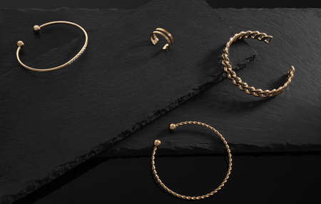 Golden jewelries three bracelets chain and spiral shape and ring on black stone platesの写真素材