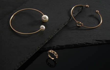 Knot shape and golden with pearls bracelets and chain shape ring on black stone platesの写真素材