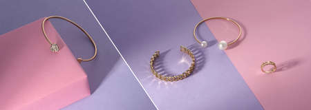 Shiny golden bracelets and chain shape ring on pink and purple background with copy spaceの写真素材