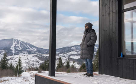 Man standing on house terrace and looking at snowy mountainsの写真素材