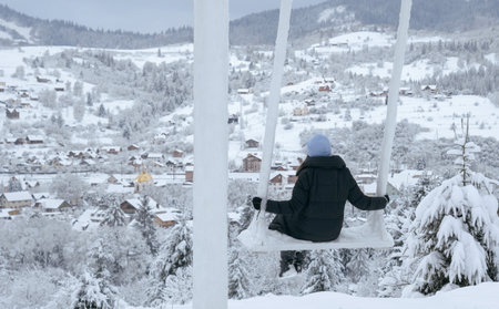 Panoramic shot of woman on swing watching view of snowy town with copy spaceの写真素材