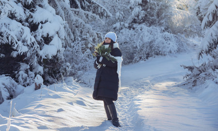 Woman in beautiful snowy forest and holding bouquet of pine tree branchesの写真素材