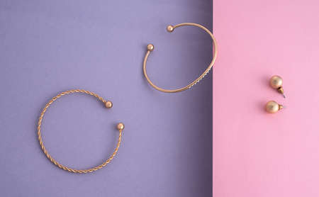 Shiny two modern bracelets and earrings pair on paper pastel color backgroundの写真素材