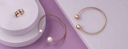 Panorama of golden pearls bracelets and ring on white platform on pink backgroundの写真素材