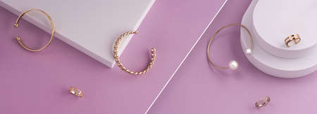 Top view of modern golden bracelets and rings on white platform on pink background with copy spaceの写真素材
