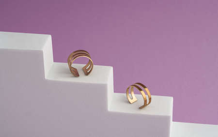 Two modern golden rings on white stairs on pink backgroundの写真素材