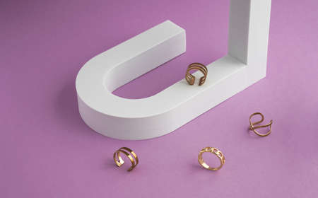 Modern golden rings collection on white u shape podium and purple backgroundの写真素材