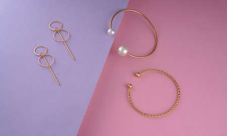 Flat lay of golden modern bracelets and earrings pair on purple and pink backgroundの写真素材
