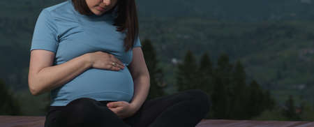 Pregnant woman hugging her tummy while sitting outdoor practicing yoga