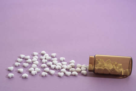 Spilled heart shaped pills bottle on purple background with copy spaceの写真素材