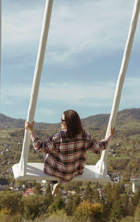 Woman on white wooden swing on mountain view in Ukraine