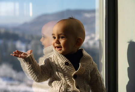 Cute baby boy sitting beside a window wearing sweaterの写真素材