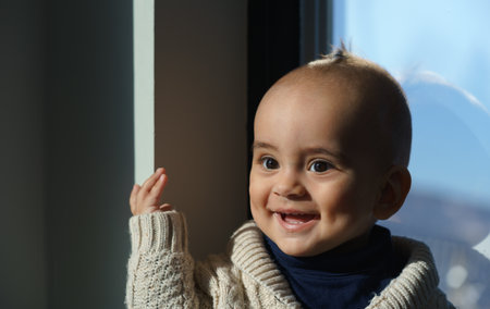 happy cute baby boy sitting beside window in sunの写真素材