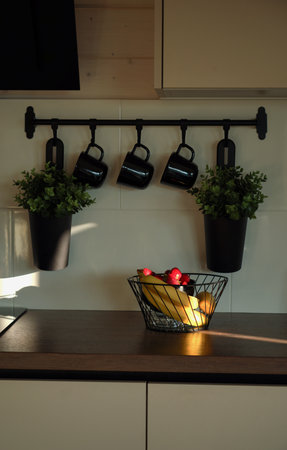 basket of fruits on kitchen counter with mugs hanged on the wallの写真素材