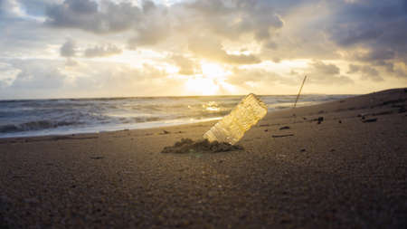 An empty trash plastic water bottle on a sand with sunrise light in the morning as background at Batu Burok Beach in Kuala Terangganu, Malaysia. Beauty landscape with dirty environment.の写真素材