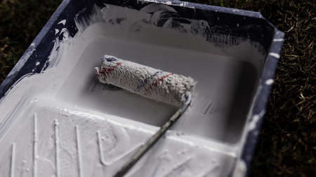 A paint roller on a plastic paint tray with a white color paint on the ground.の写真素材