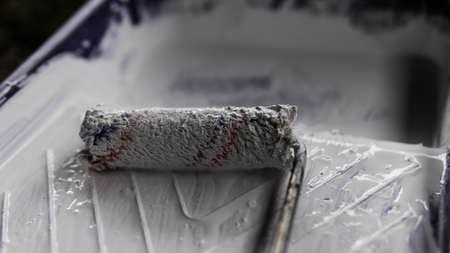 A paint roller on a plastic paint tray with a white color paint on the ground.の写真素材