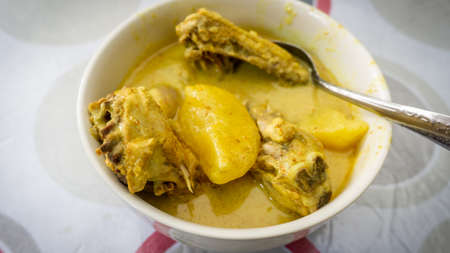 Ayam Masak Lemak Cili Api/ Chicken stew in coconut milk- traditional Malay cuisine in white bowl on table. Add with potatoes and turmeric. Homemade dish. Common food for lunch. Spicy and creamy taste.の写真素材