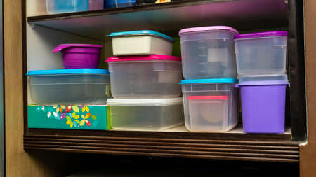 Piles of plastic container for food storage neatly arranged on a kitchen cabinet. Colorful food...