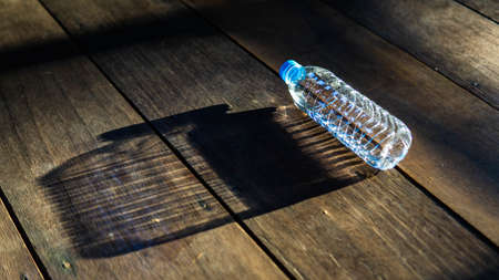 Sunlight rays from outside reflected onto small plastic bottle on the wooden floor and formed a big...