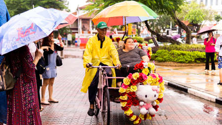 Malacca City, Melaka - June 26, 2019: A local man riding his beautiful and colorful rickshaw with a Caucasian tourist go visit around Malacca City during the rainy day.のeditorial素材