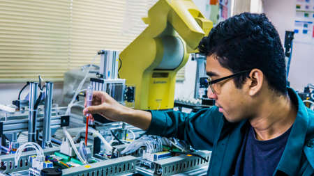 A young Malay engineering student with spectacles working in the lab repairing and troubleshooting...