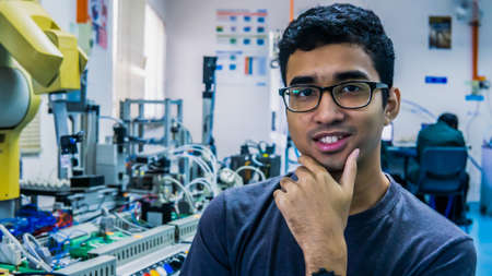 A young Malay engineering student with spectacles working in the lab and thinking by holding chin...
