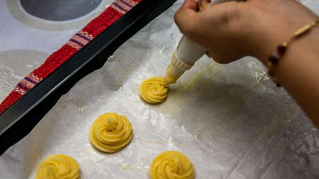 Close up view of girl making cream puff pastry ball using the piping bag in a row before baking it...