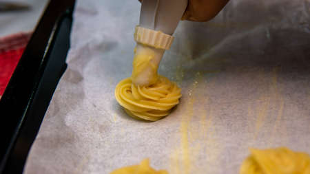 Close up view of girl making cream puff pastry ball using the piping bag in a row before baking it...