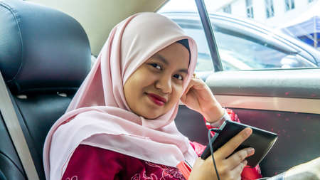 Portrait of Malay Asian muslim teenager girl using earphone listening to music or watch online video...