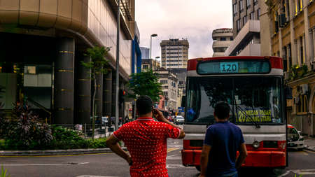 Unidentified local person in red casual clothing is on the phone at the street of Kuala Lumpur. Red bus picking up passenger at the road side.のeditorial素材